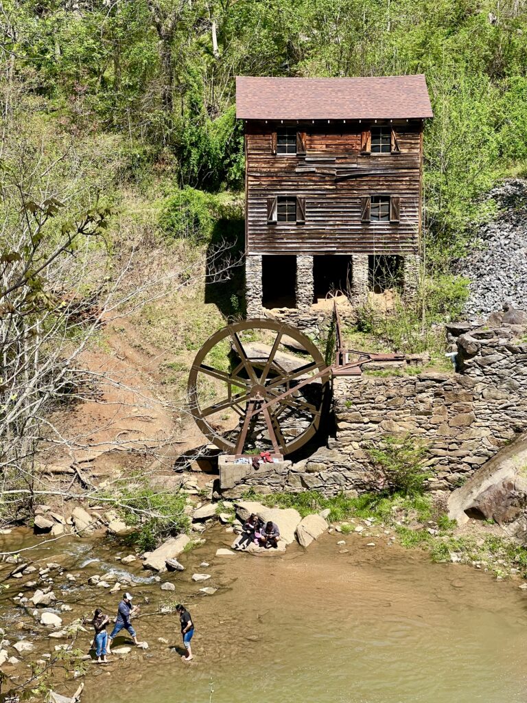 meytre grist mill at mcgalliard falls park as seen from above, with some people standing in the water in front of it